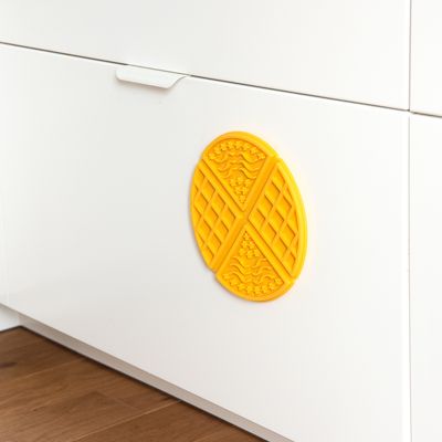 Juguete ovalado amarillo con superficies texturadas, fijado a una puerta de armario blanca. Adecuado para juego interactivo o entretenimiento.