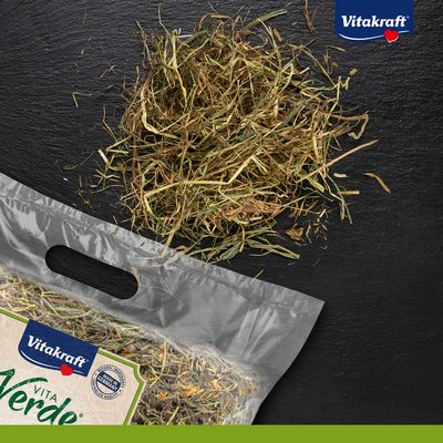 Vitakraft Vita Verde siano w przezroczystym opakowaniu z luźnym sianem obok. Certyfikat: Made in Germany, naturalna jakość.