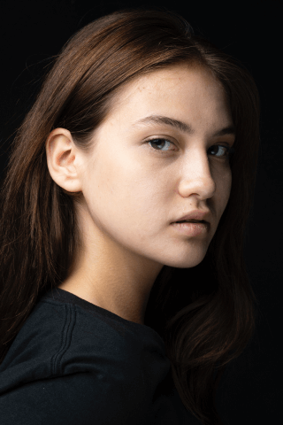 A woman with long brown hair wearing a black shirt, exuding elegance and confidence.