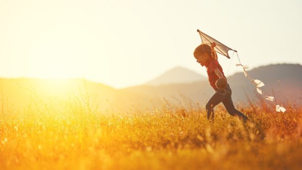 child running on a field holding a kite