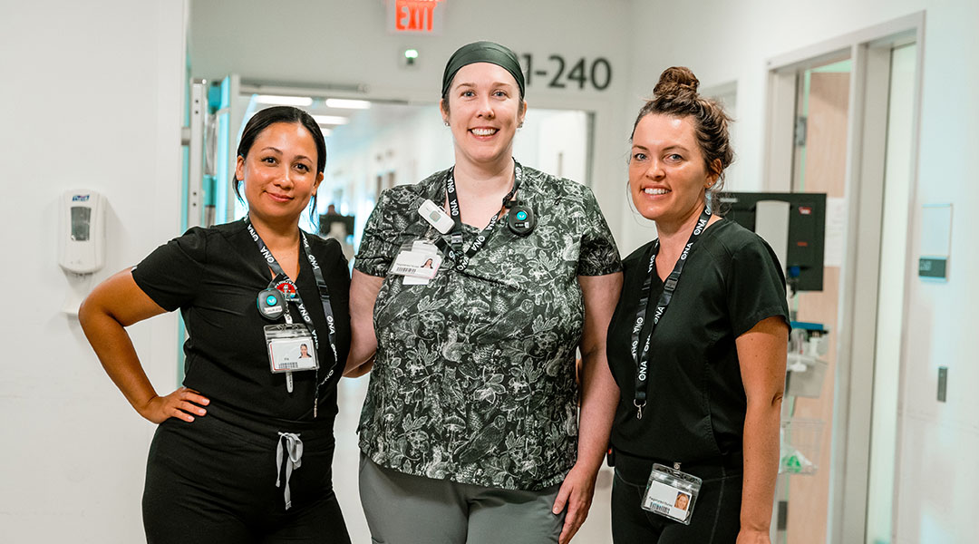 Three nurses standing in a hospital hallway, smiling.