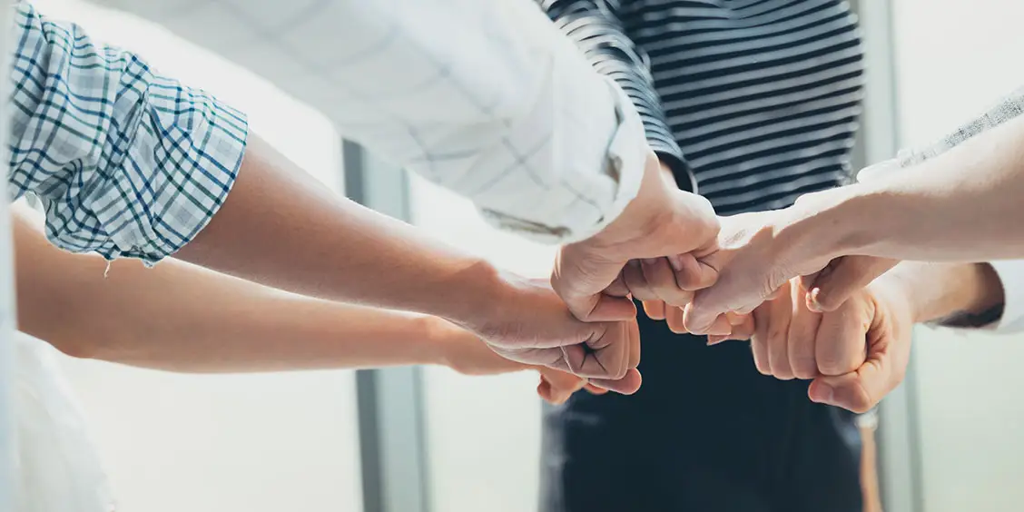 A group of people doing a fist bump in a circle, symbolizing teamwork and collaboration, related to IT maintenance support services.