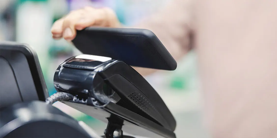 A person uses a smartphone to make a contactless payment at a card reader.