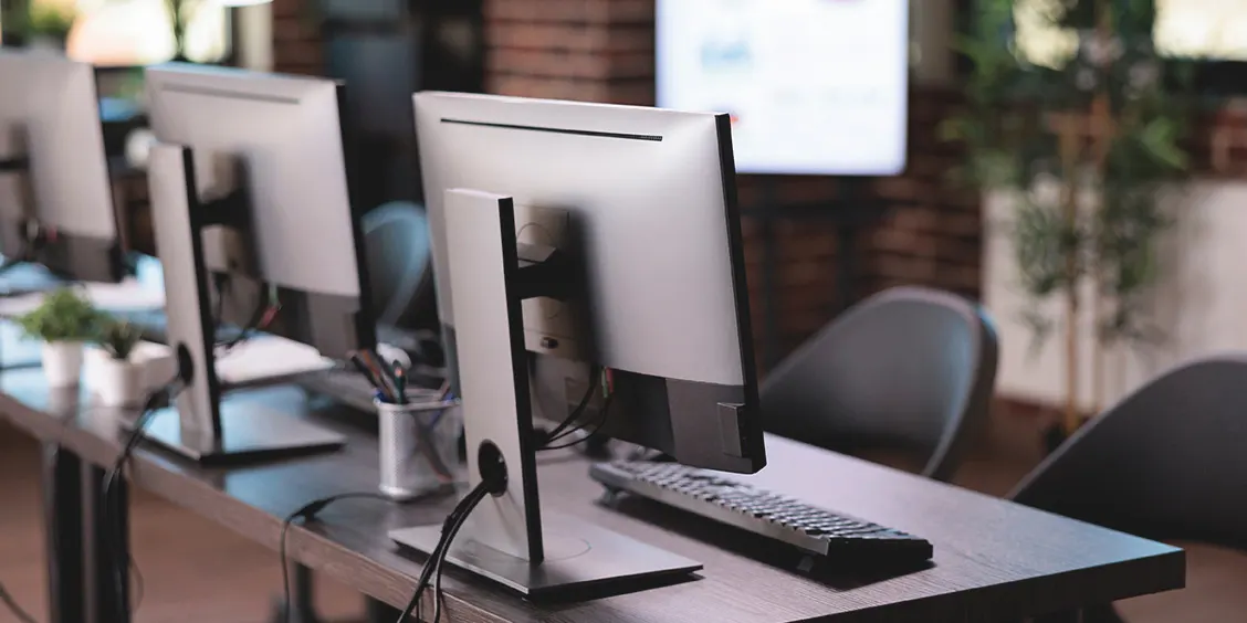Rows of computers on a modern office desk, highlighting IT maintenance support services setup.