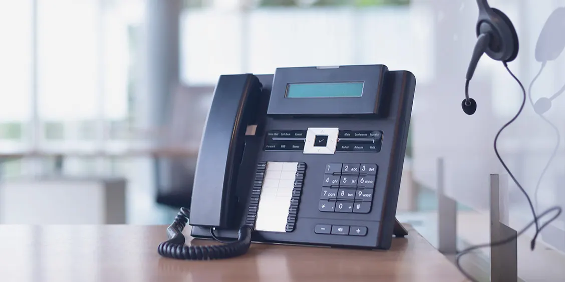 Office phone on desk with headset nearby, representing IT support services at Piccola Tech.