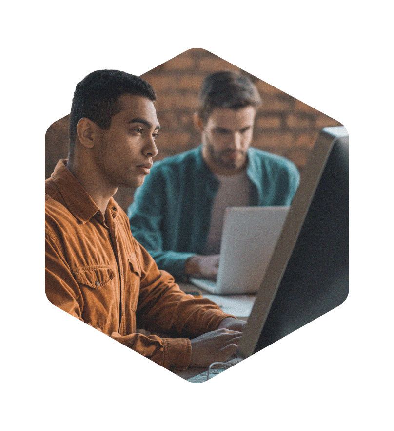 A photo masked in a hexagon of two male developers working on computers