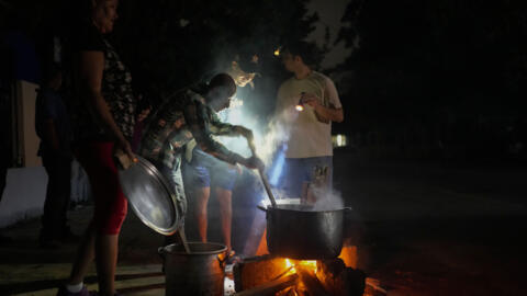 Vecinos cocinan con leña en un fuego improvisado en la calle la noche del sábado 19 de octubre de 2024 en La Habana, Cuba, donde sufren cortes de luz desde el viernes.