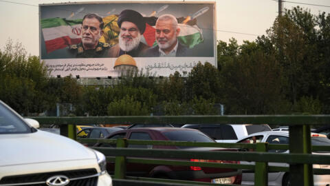 Des véhicules passent devant un panneau d'affichage sur une autoroute à Téhéran, Iran, lundi 7 octobre 2024, montrant le chef du Hezbollah Hassan Nasrallah, au centre, le chef du Hamas Ismail Haniyeh,