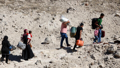 Personas huyen de los bombardeos israelíes pasando por un cráter causado por un ataque israelí en la zona de Masnaa.