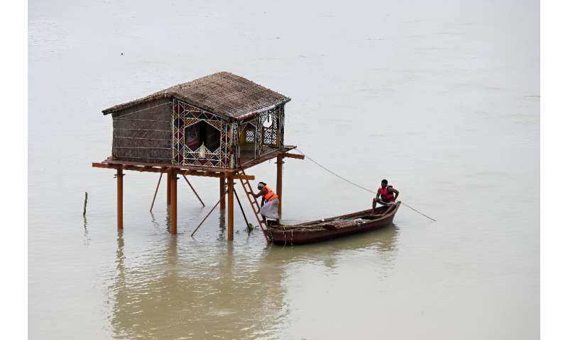 Men row a boat near a deluged straw hut in the river Ganges in Prayagraj: in India, just months after the country baked in its longest-ever heatwave, ferocious rainstorms have triggered widespread flooding and landslides