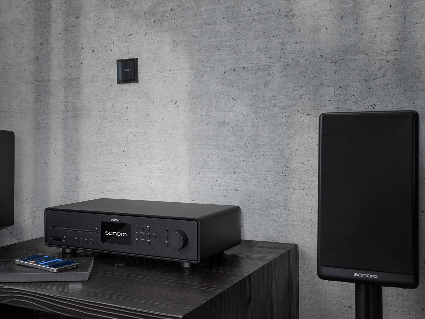 Sonoro AVATON - modernes High-End Musiksystem in Schwarz mit passendem Lautsprecherset, elegant inszeniert vor Betonwand.
