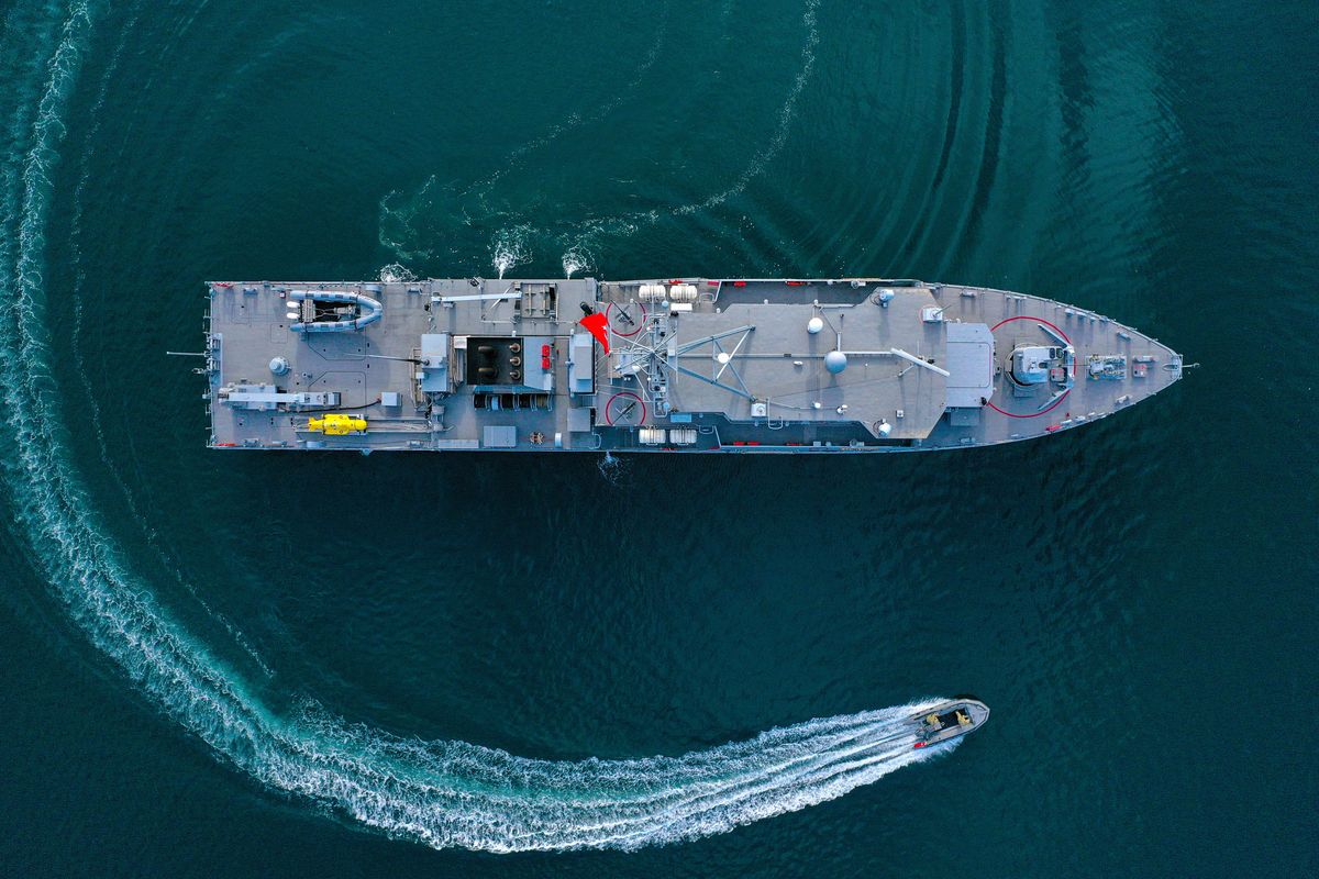 An aerial view of a large ship floating in blue water and a smaller boat circling around it