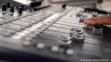 A hand pushes some sliders on a sound mixer