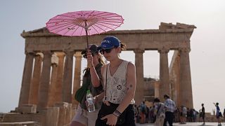 Туристы с зонтиком прогуливаются перед Парфеноном на древнем Акрополе в центре Афин, среда, 12 июня 2024 года. 