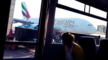 A woman in a bus looks out at an Emirates Airbus A380 jumbo jet at Dubai International Airport in Dubai, United Arab Emirates, Friday, Sept. 9, 2022. 