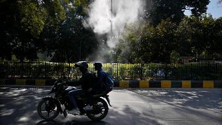 Um motociclista passa por aspersores que pulverizam água na esperança de assentar a poeira e acalmar a poluição do ar em Nova Deli, a 12 de fevereiro de 2025.