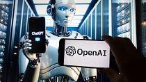 The OpenAI logo is seen displayed on a cell phone with an image on a computer screen generated by ChatGPT's Dall-E text-to-image model, Friday, Dec. 8, 2023, in Boston