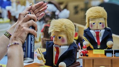 Uma mulher usa spray de cabelo para fixar o cabelo de um quebra-nozes intitulado 'Mesa Resoluta do Presidente' na fábrica Steinbach-Volkskunst em Marienberg, 15 de abril de 2025