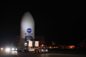 A large rocket fairing containing NASA’s Nancy Grace Roman Space Telescope rests on a platform tugged by a truck as it approaches integration with its rocket for launch.