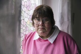 Eine Frau mit rosa Pullover schaut in die Kamera