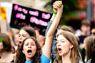 Zwei jugendliche Demonstrantinnen halten sich an den Händen und rufen