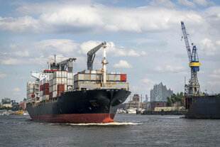 Ein Containerschiff im Hamburger Hafen mit Kränen und Stadtbild im Hintergrund