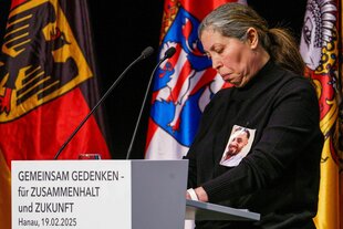 Eine Frau, in Schwarz gekleidet, steht traurig an einem Rednerpult