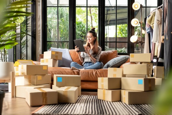 Woman talking on phone, sitting on couch, surrounded by shipping boxes