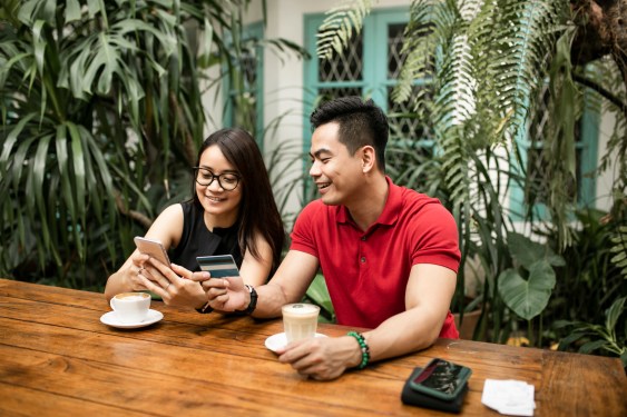 Couple at cafe shopping online while man holds credit card both smiling, used in post about Skorlife