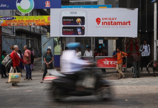 A man rides a bike past a bus stop with an advertisement for Swiggy Instamart in Mumbai, India.