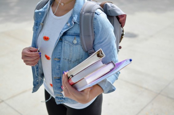 woman wearing blue denim jacket holding textbooks