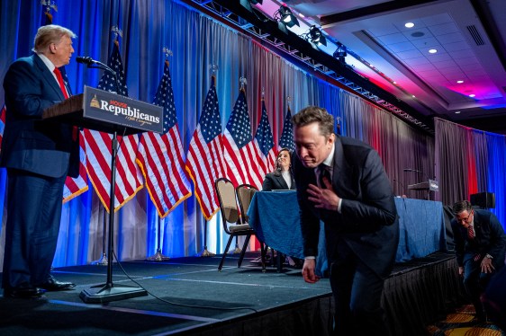 Elon Musk walking past stage while Donald Trump stands at the podium