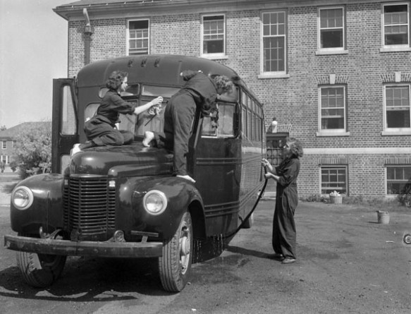 A black-and-white photograph of two members of the Women’s Royal Canadian Naval Service washing the front of a bus while their colleague sprays the side of the bus with a hose.