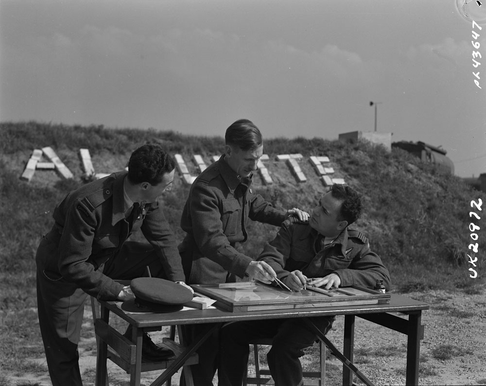 By an English airstrip, three Air Force officers planning while looking over a table with maps.