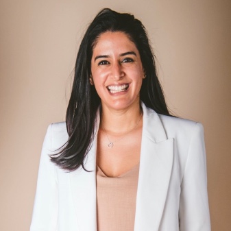 A smiling woman in a white blazer and tan top.