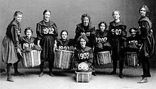 Photo en noir et blanc d'une équipe de joueuses de basketball en uniforme floqué de la date « 1902 ».