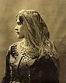 Woman wearing an ornately embroidered jacket known as Karakou, head scarf, heavy necklace and Khit errouh