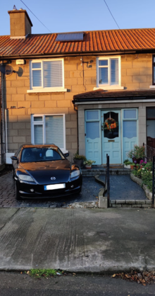 A garden with a car in it, fence taken away for car access, small gate for pedestrian access which would of been there at the start. Sunny afternoon.