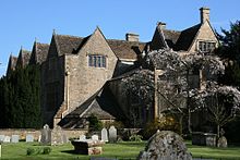 Old mansion house with triangular roofs. In the foreground is a graden with gravestones.