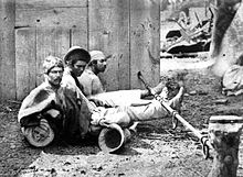 Trio of men seated on the ground with ankles shackled to a pole lying horizontally