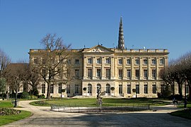 Photographie d'un grand bâtiment en pierre entouré d'herbe verte et de quelques arbres.