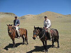 Un couple occidental sur des chevaux mongols, souriant.