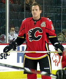 A Calgary Flames player observes his teammates who are off camera. On his uniform is a small patch that uses Atlanta's "Flaming A" logo to denote his position as an alternate captain.