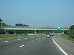 Ground-level view of a three lanes of a divided freeway; a large green and gray overpass bridge and a green exit sign are visible in the distance.