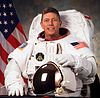 man in space suit holding helmet, American flag in background