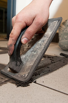 Colour photograph of non-shrink grout being applied to white floor tiles