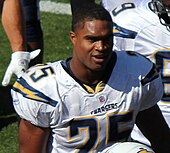 An American football player looks forward. He is wearing a white jersey with the number 25 across the chest. He is not wearing his helmet.