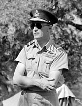 Outdoor half portrait of man in light-coloured military uniform with peaked cap, wearing sunglasses