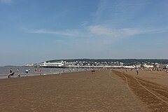 Multiple houses and other buildings around a bay into which a pier projects. On the background are hills