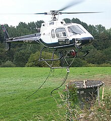 Hubschrauber mit Streubehälter hebt zur Waldkalkung ab